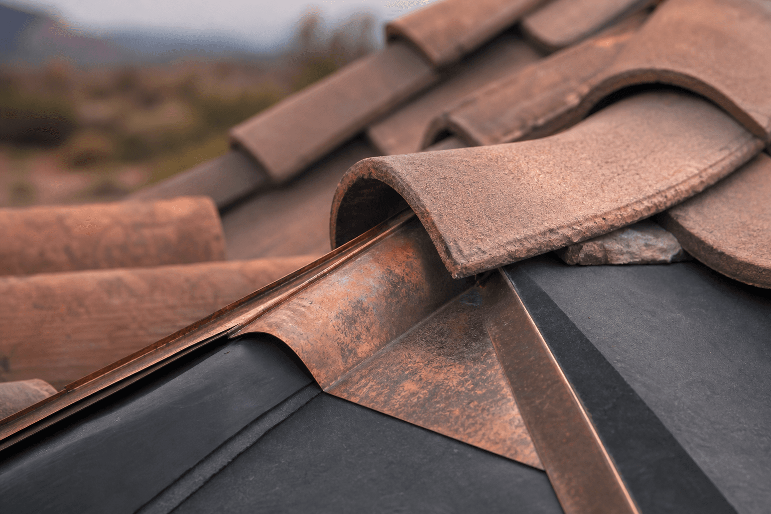Close view of roof tile, ridge, and copper flashing installed with precision.